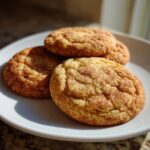 Close-up of three chewy snickerdoodles generously coated in cinnamon sugar resting on a white plate.