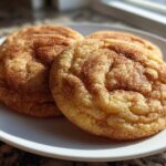 Close-up of three perfectly chewy snickerdoodles coated in cinnamon sugar resting on a white plate.