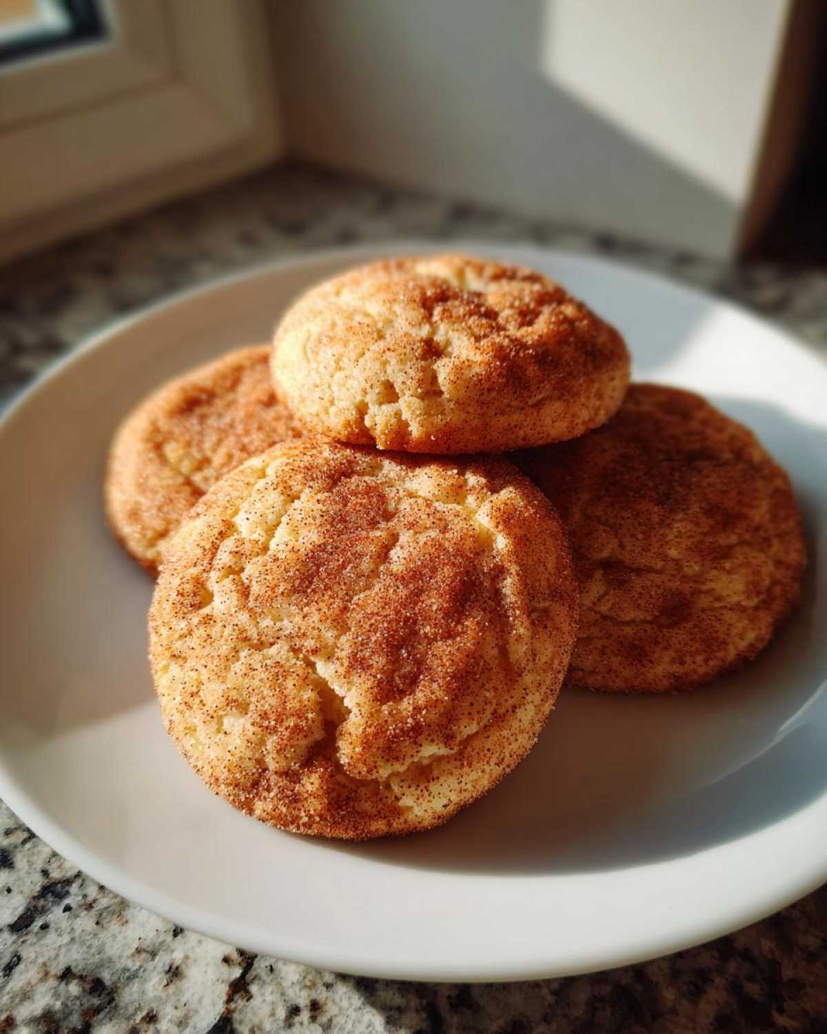 Four freshly baked, chewy snickerdoodles generously coated in cinnamon sugar, stacked on a white plate.