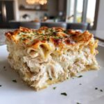 A generous slice of rich chicken alfredo lasagna showing layers of shredded chicken, creamy sauce, and pasta, topped with melted, browned cheese and parsley.