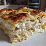 A thick, layered slice of chicken alfredo lasagna featuring shredded chicken, creamy sauce, and a bubbly, browned cheese top.