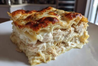 A thick, layered slice of chicken alfredo lasagna featuring shredded chicken, creamy sauce, and a bubbly, browned cheese top.