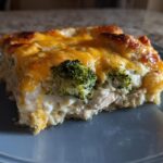 A square serving of creamy Chicken Divan casserole topped with melted cheddar cheese and visible broccoli florets.