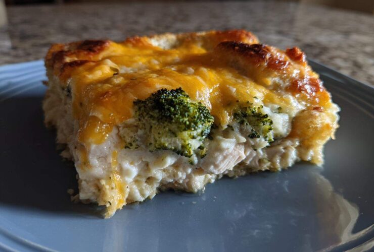 A square serving of creamy Chicken Divan casserole topped with melted cheddar cheese and visible broccoli florets.