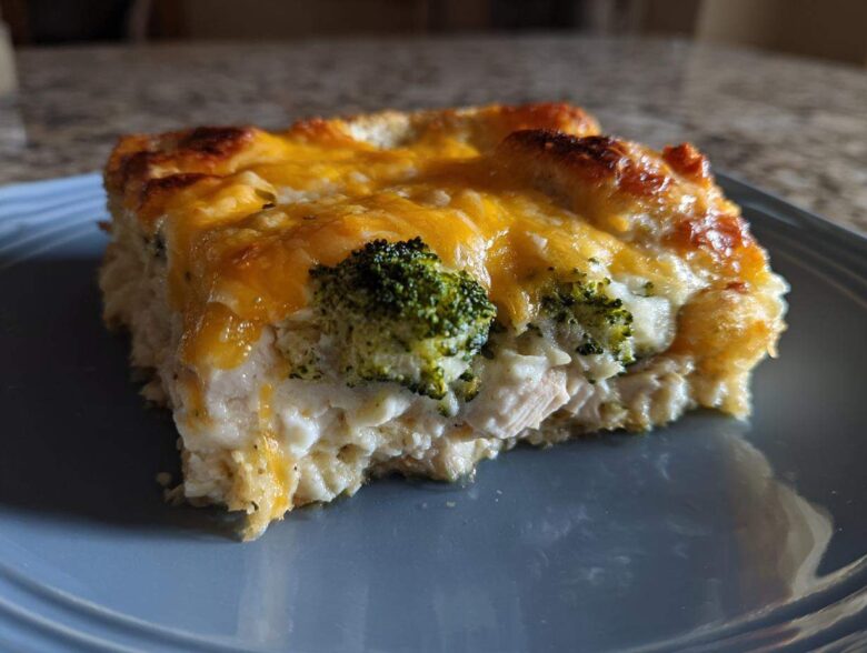 A square serving of creamy Chicken Divan casserole topped with melted cheddar cheese and visible broccoli florets.