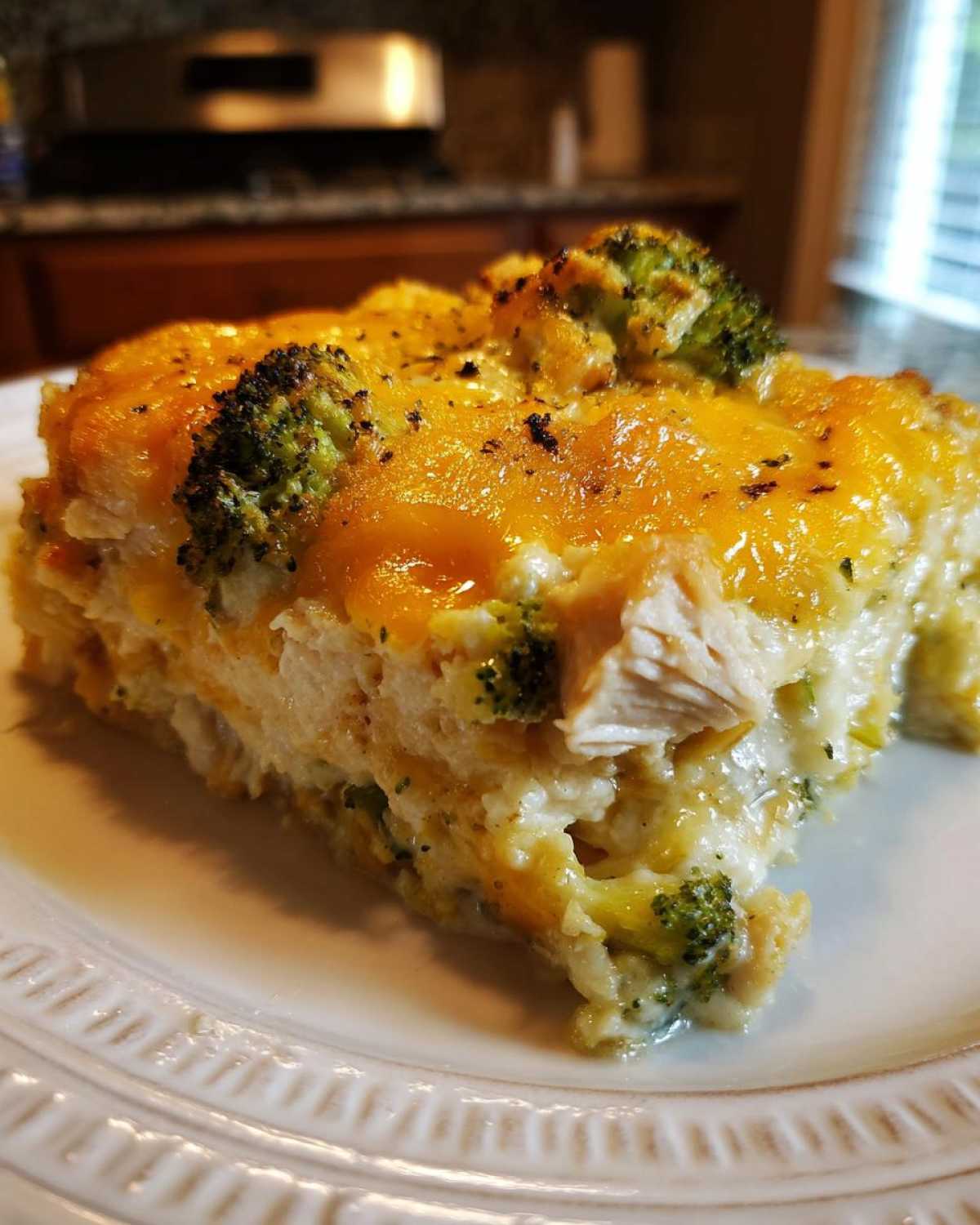 A close-up of a rich slice of Chicken Divan casserole topped with melted cheddar cheese and broccoli florets.