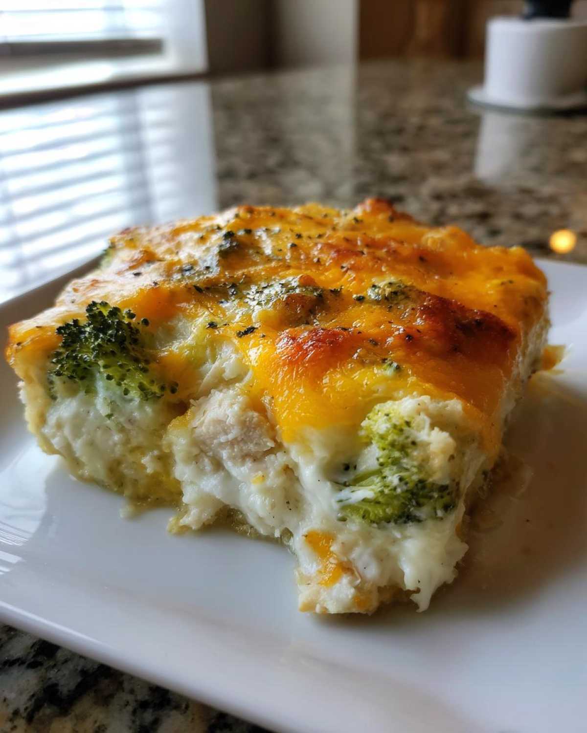 A close-up of a square serving of Chicken Divan with creamy sauce, chicken chunks, and broccoli, topped with melted cheddar cheese.