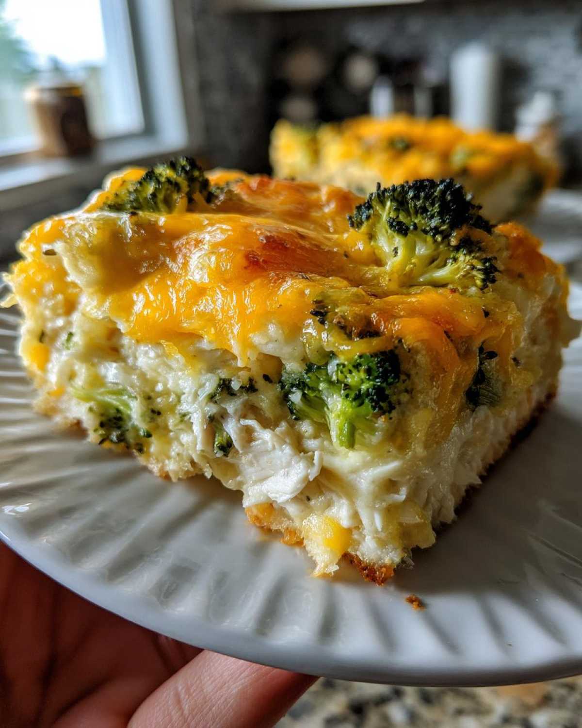A close-up of a square serving of creamy Chicken Divan casserole topped with melted cheddar cheese and broccoli florets.