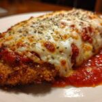 Close-up of a perfectly cooked chicken parmesan recipe cutlet, golden brown and crispy, covered in melted mozzarella and marinara sauce.