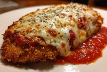Close-up of a perfectly cooked chicken parmesan recipe cutlet, golden brown and crispy, covered in melted mozzarella and marinara sauce.