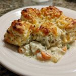 A close-up serving of creamy chicken pot pie casserole topped with golden, cheesy biscuits.