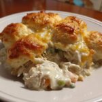 A serving of creamy chicken pot pie casserole topped with golden brown biscuits on a white plate.