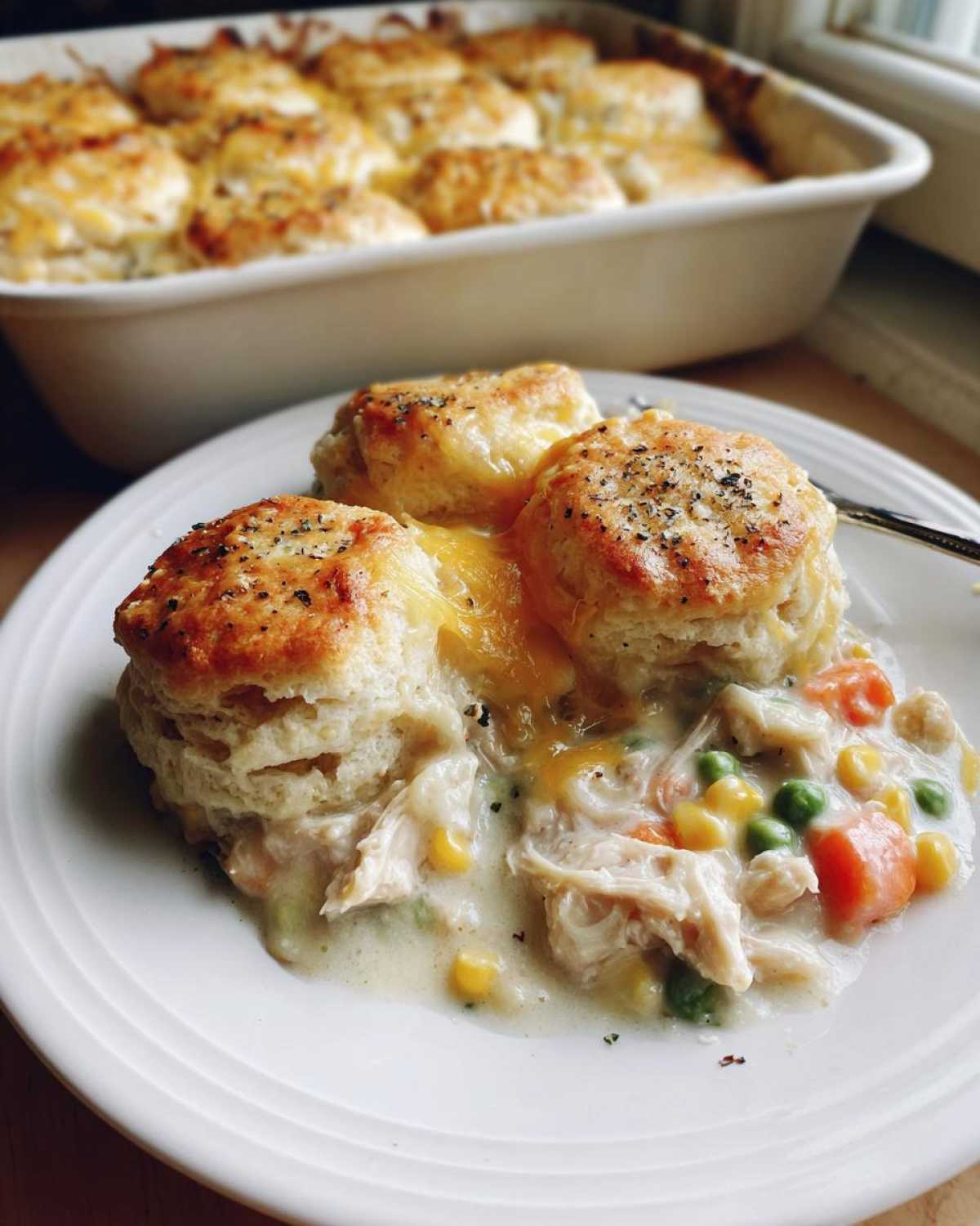 A serving of creamy chicken pot pie casserole topped with golden biscuits and melted cheese.