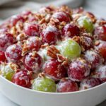 Close-up of creamy chicken salad chick grape salad featuring red and green grapes coated in dressing and topped with pecans.