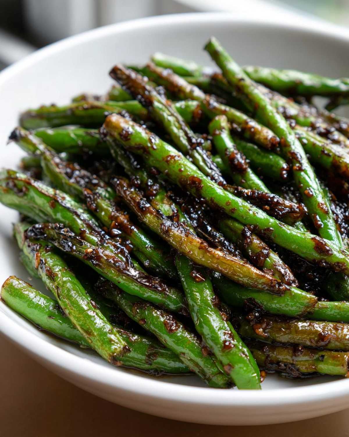 Close-up of vibrant green beans coated in a dark, glossy garlic sauce, ready to serve.