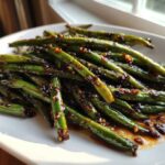Close-up of vibrant Chinese green beans with garlic sauce, glistening under natural light.