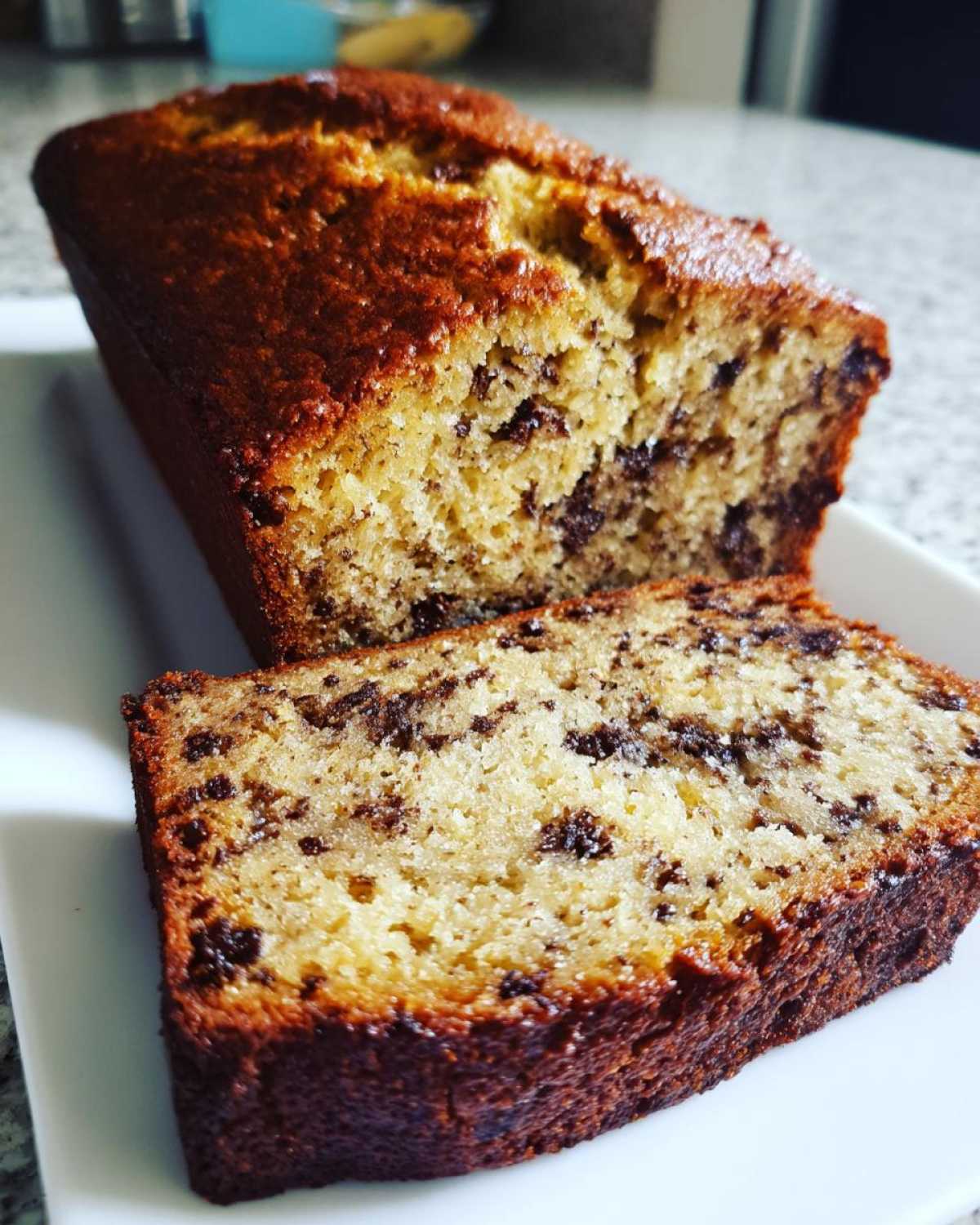 A close-up of a chocolate chip vegan banana bread loaf with one thick slice cut and resting in front.