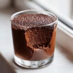 Close-up of rich, airy chocolate mousse in a glass with a bite taken out, showing the texture.