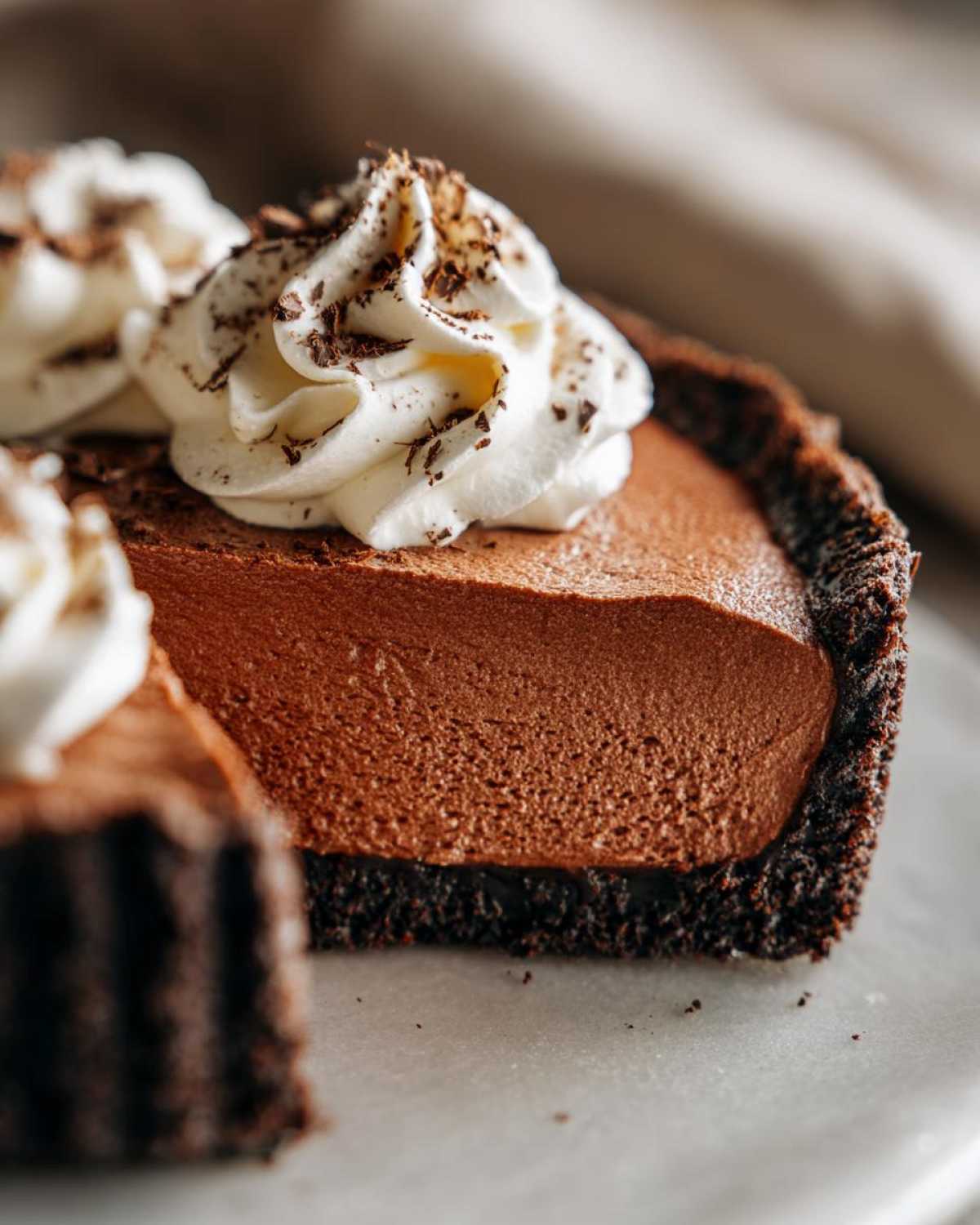 Close-up of a slice of rich chocolate mousse pie showing the airy filling, dark crust, and whipped cream topping.