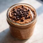 Close-up of rich chocolate overnight oats in a glass jar, topped generously with dark chocolate chips.
