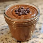 Close-up of creamy chocolate overnight oats topped with mini chocolate chips in a glass jar.