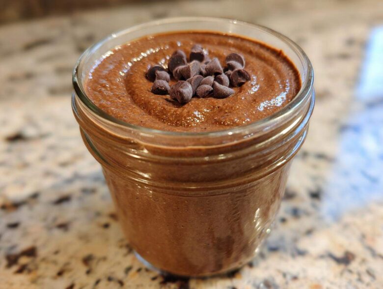 Close-up of creamy chocolate overnight oats topped with mini chocolate chips in a glass jar.
