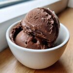 Two scoops of rich, dark chocolate protein ice cream sprinkled with sea salt in a small white bowl.