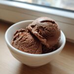Two scoops of rich chocolate protein ice cream served in a small white bowl.