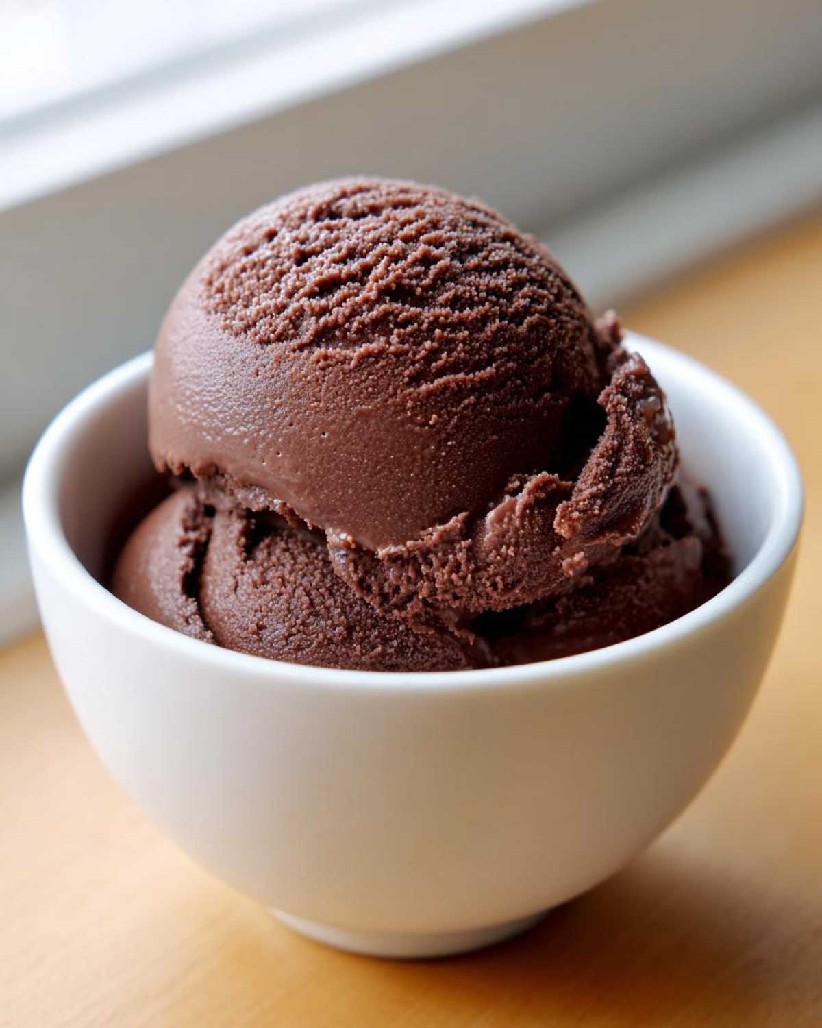 Two scoops of dark chocolate protein ice cream served in a small white bowl.