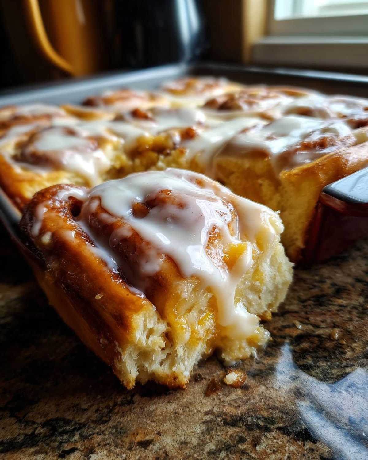 A close-up shot showing a piece of soft, gooey cinnamon roll casserole drizzled heavily with white icing.