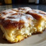 A close-up of a soft, baked portion of cinnamon roll casserole drizzled with white icing.