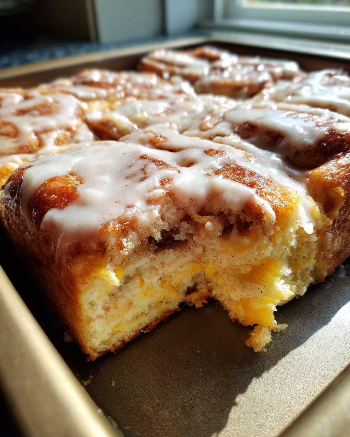A close-up photo of a freshly baked cinnamon roll casserole with thick white icing, showing a piece taken out.
