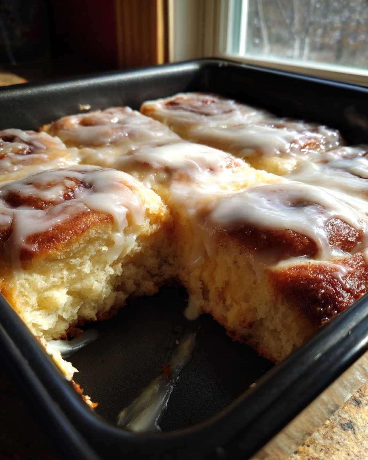 A pan of freshly baked Cinnamon Roll Casserole with a piece removed, drizzled generously with white icing.
