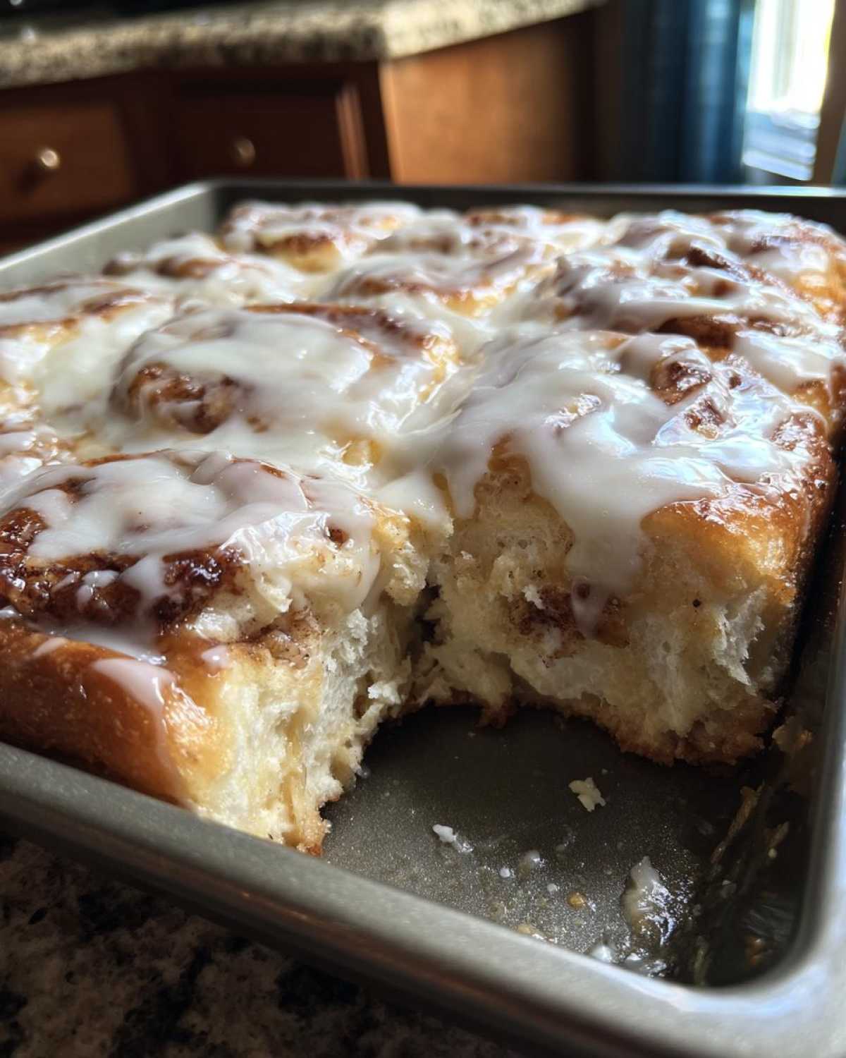 Close-up of a pan of gooey Cinnamon roll casserole with white icing, showing a piece removed.