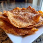 A stack of crispy, fried buñuelos generously coated in cinnamon sugar, resting on a white rectangular plate.