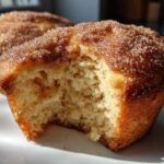 A close-up shot of a cinnamon sugar french toast muffin with a bite taken out, showing the soft, fluffy interior.