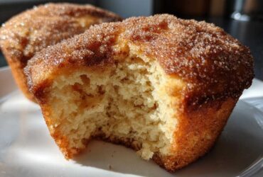 A close-up shot of a cinnamon sugar french toast muffin with a bite taken out, showing the soft, fluffy interior.