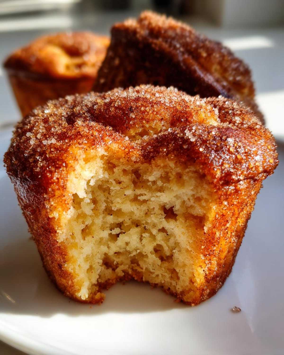 Close-up of a cinnamon sugar french toast muffins with a bite taken out, showing the soft interior.