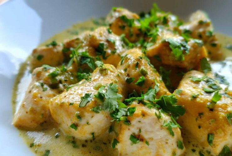 Close-up of tender coconut lime chicken pieces coated in a creamy, yellow-green sauce and topped with fresh parsley.