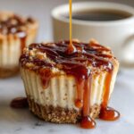 Close-up of a cookie butter cheesecake cup being drizzled with thick caramel sauce, with coffee in the background.
