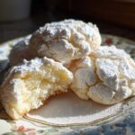 Close-up of soft, powdered sugar-dusted cool whip cookies, one broken open to show the texture.