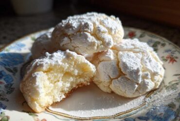 Close-up of soft, powdered sugar-dusted cool whip cookies, one broken open to show the texture.