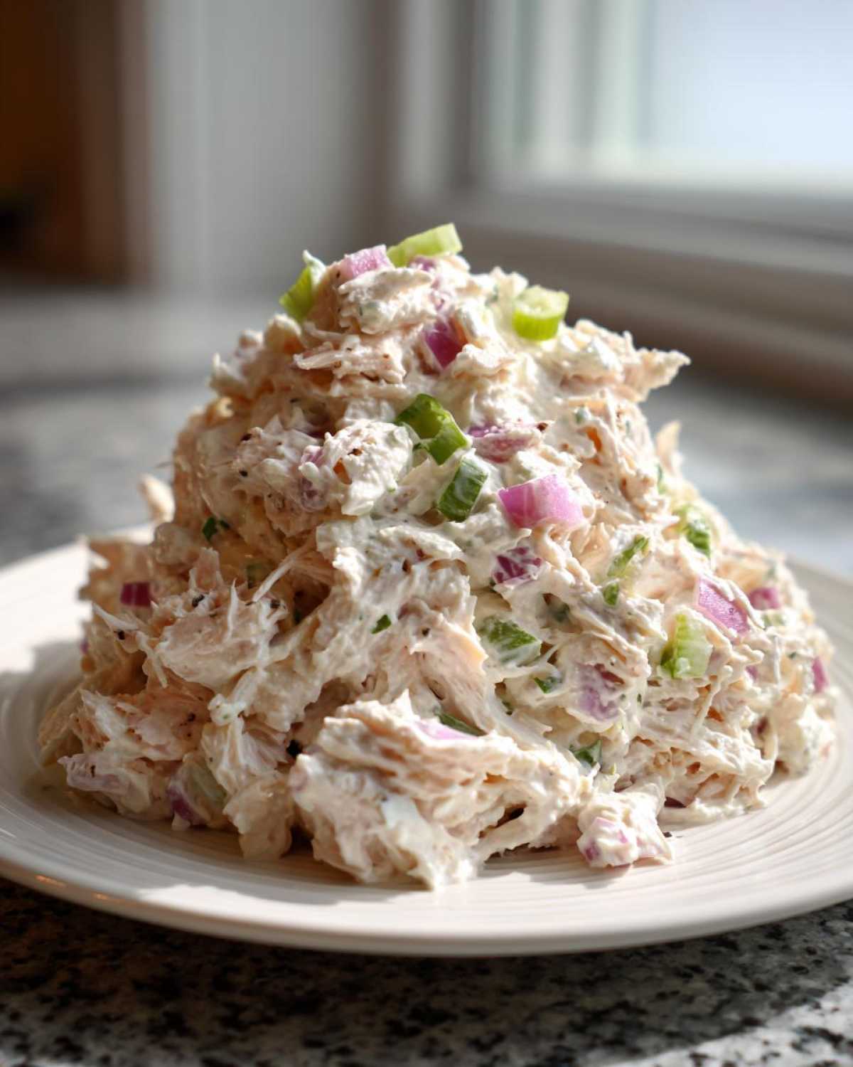 A generous mound of creamy cottage cheese chicken salad mixed with red onion and celery on a white plate.