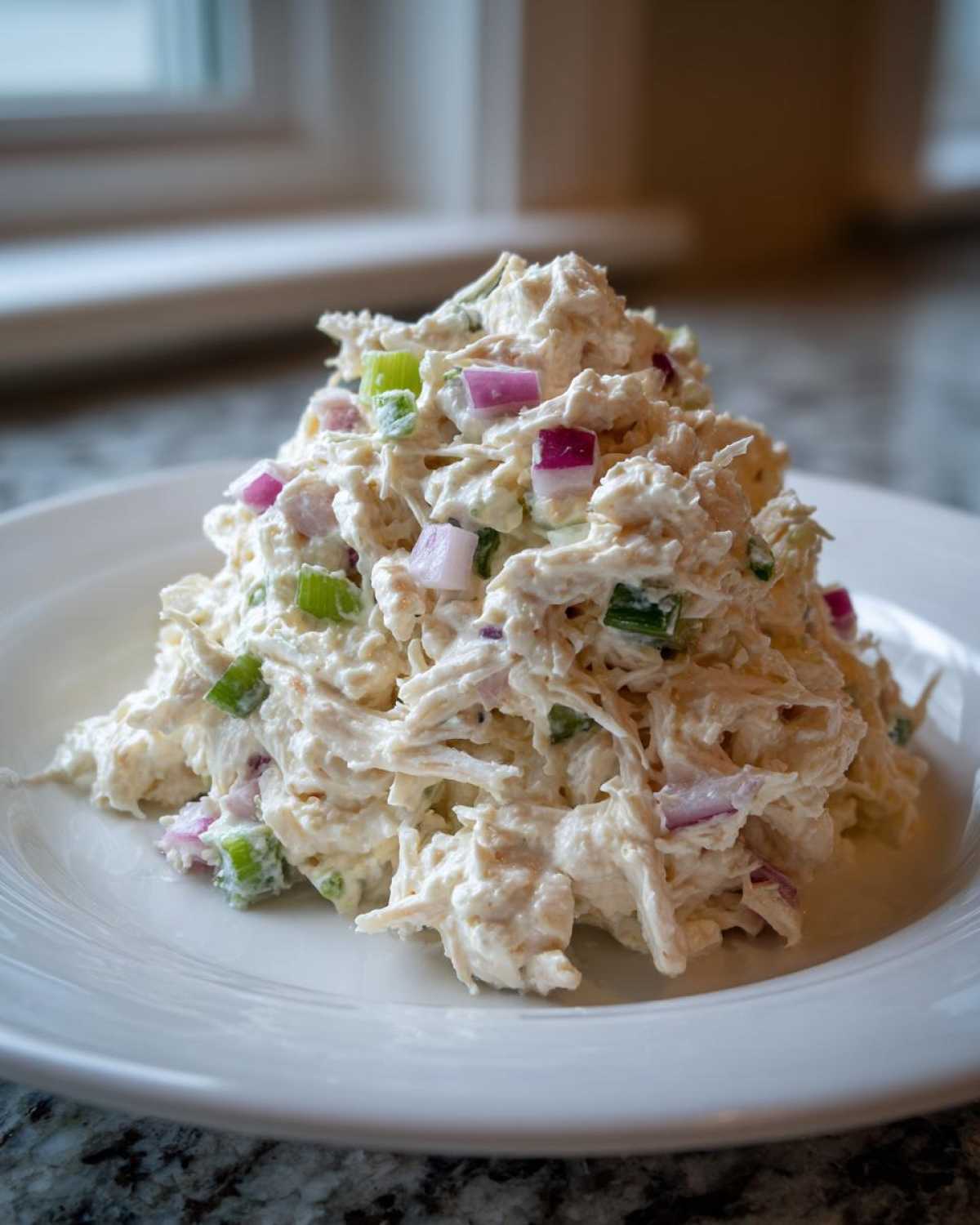 A mound of creamy cottage cheese chicken salad mixed with diced red onion and celery on a white plate.