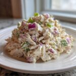A mound of creamy cottage cheese chicken salad mixed with visible chunks of red onion and green scallions, served on a white plate.