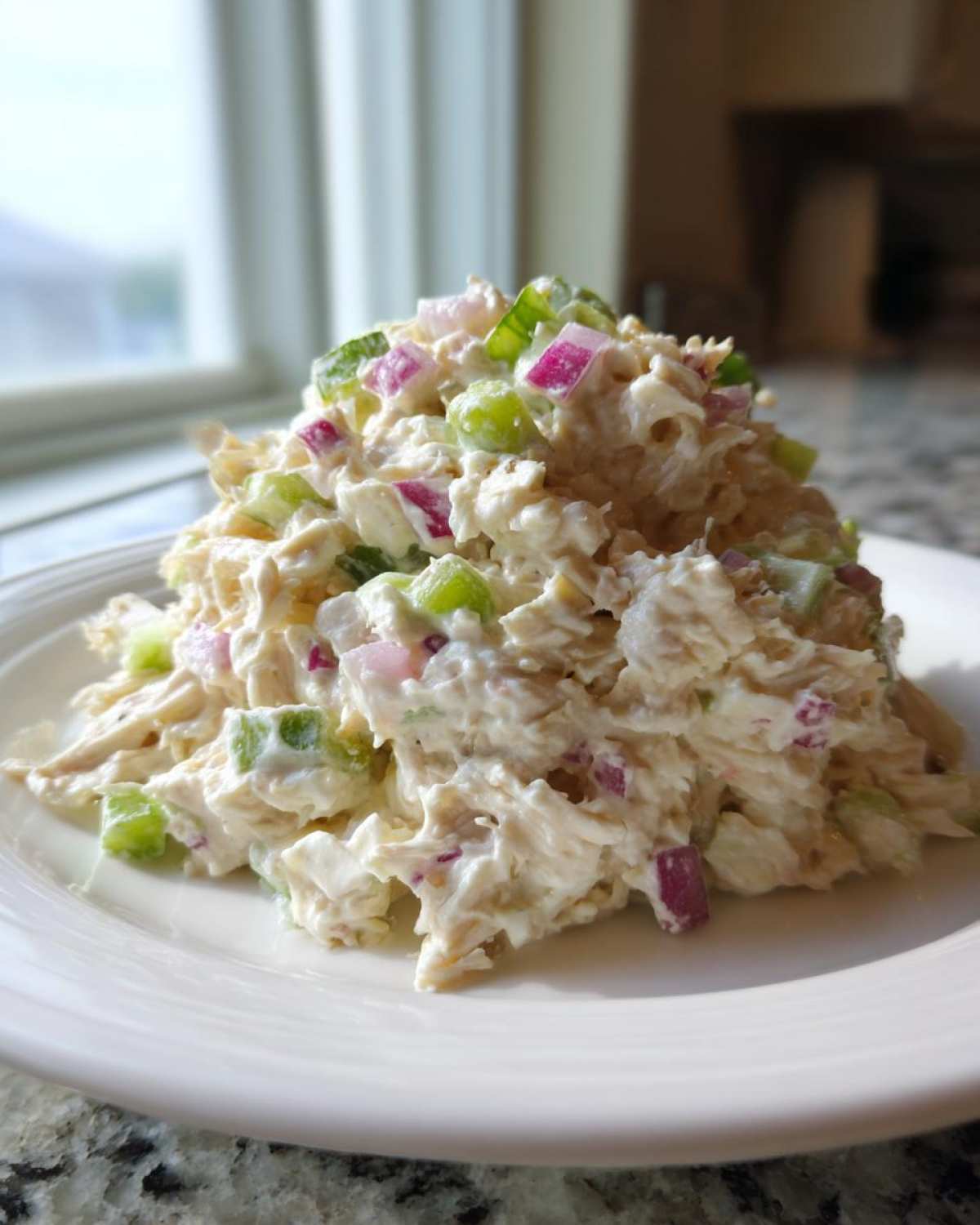 A mound of creamy cottage cheese chicken salad mixed with diced celery and red onion served on a white plate.