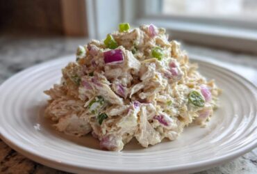 A mound of creamy cottage cheese chicken salad mixed with visible chunks of red onion and green scallions, served on a white plate.