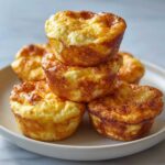 A stack of five golden brown cottage cheese egg cups, resembling mini frittatas, served on a white plate.