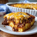 A hearty slice of cowboy cornbread casserole topped with savory chili and melted cheddar cheese.