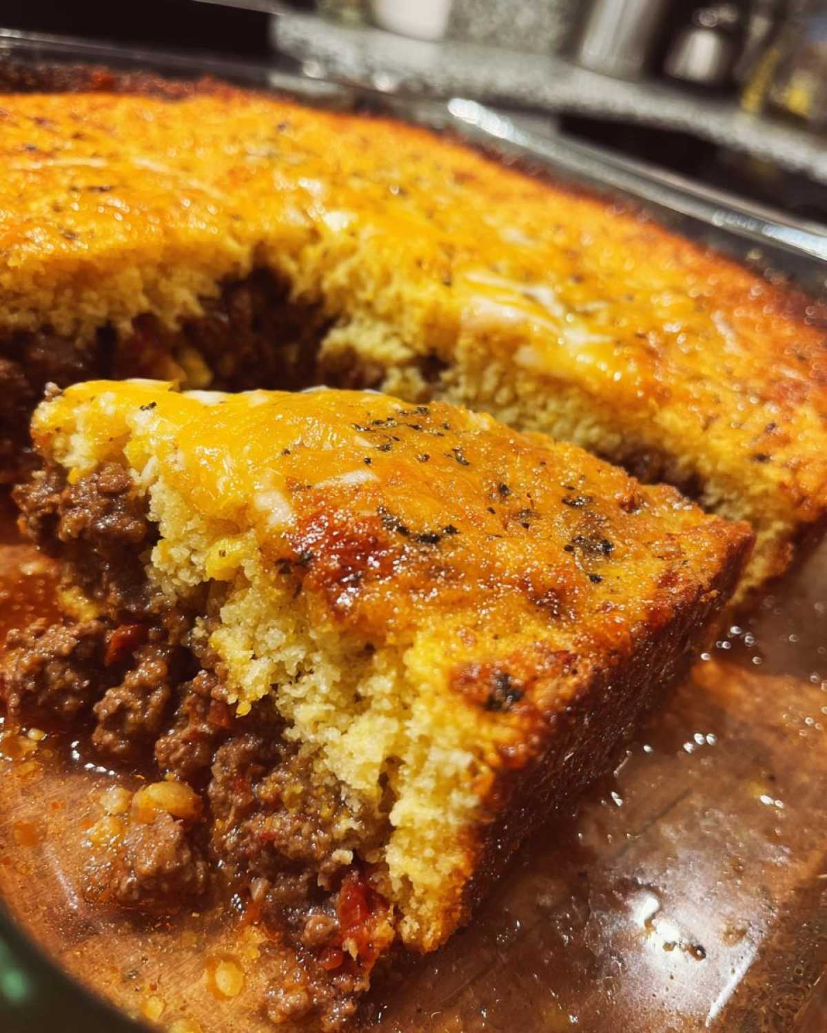 Close-up of a serving of cowboy cornbread casserole showing a thick layer of cheesy cornbread over a savory ground meat filling.
